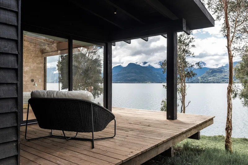 Covered timber deck with black columns and exposed beams overlooking a lake and distant mountains
