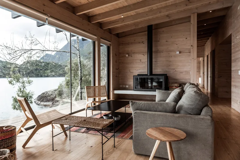 Living room with horizontal timber cladding, exposed ceiling beams, and floor-to-ceiling glazing facing the water