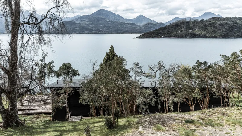 Lake-facing elevation partially screened by native trees with mountains visible across the water