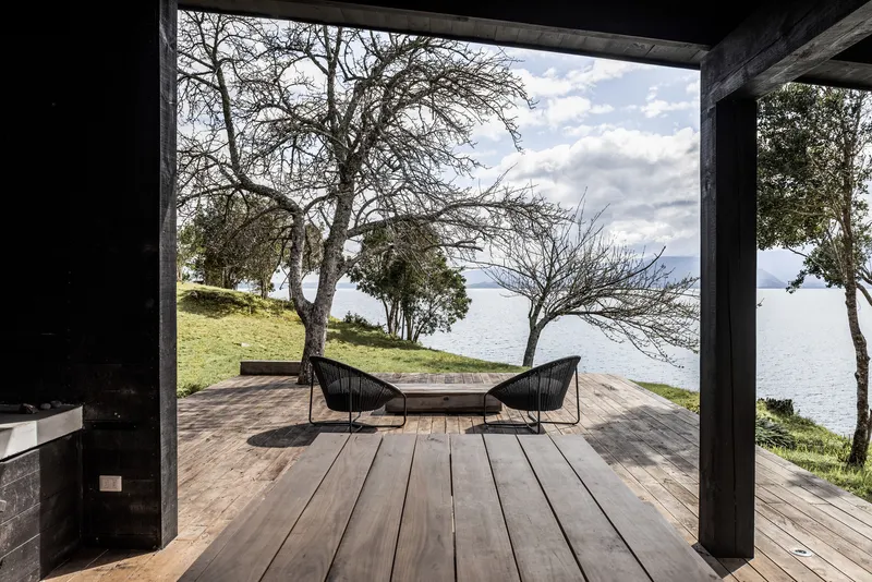 Timber deck terrace framed by dark columns with two chairs facing trees and a lake