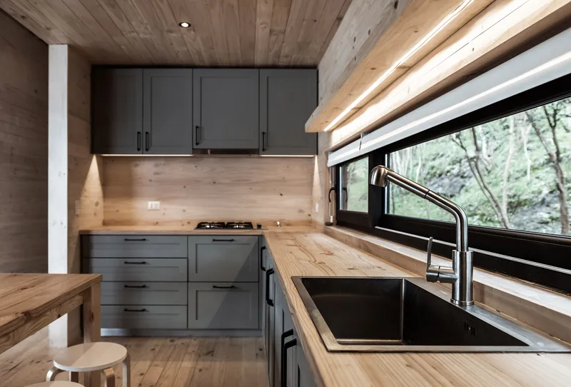 Kitchen with timber countertops, dark grey cabinetry and wood ceiling with view to forested hillside