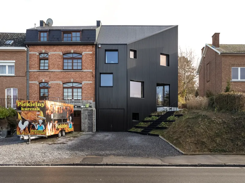 Street view of the black corrugated metal facade nestled between brick buildings with a food truck parked in front