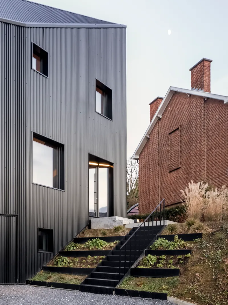 Exterior view showing the terraced planted beds ascending black steel stairs toward the rear entrance