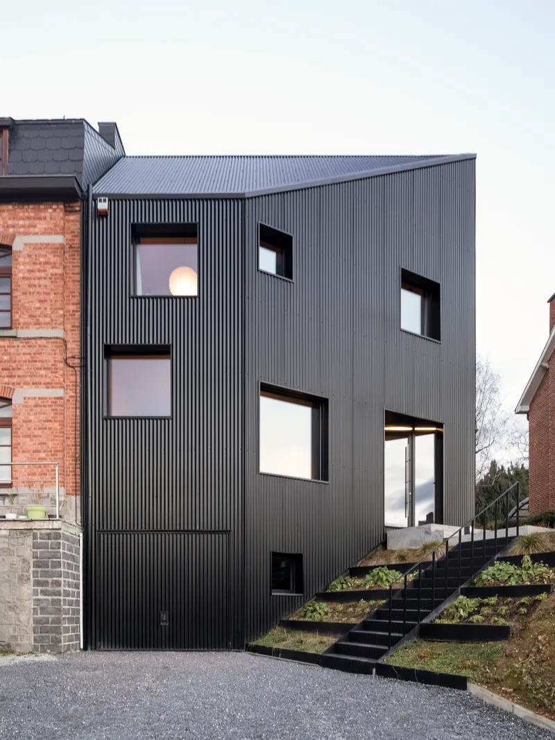 The vertical corrugated cladding and punched window openings adjacent to the planted terraced landscape