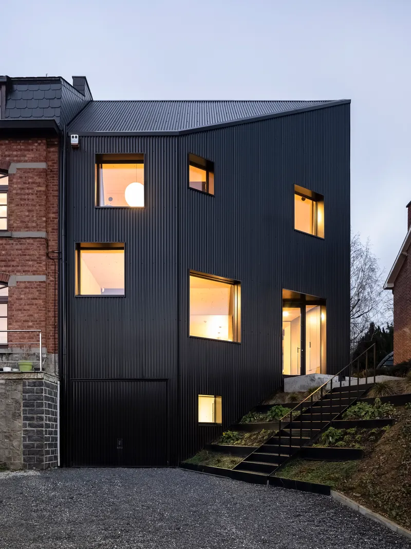 The facade with illuminated interior spaces visible through scattered window openings at dusk