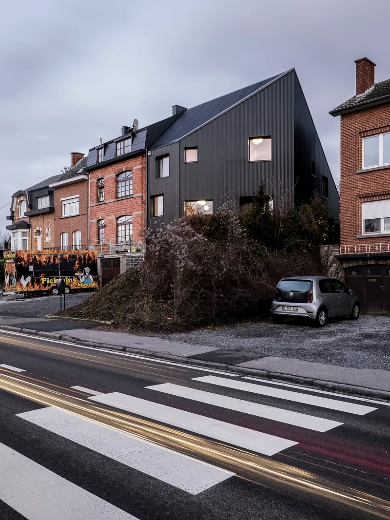 Street view of the dark corrugated metal facade rising above neighboring brick houses under an overcast sky