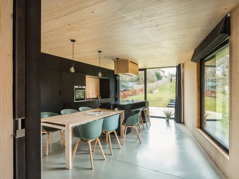 Open-plan dining area with pale timber ceiling, black cabinetry, and floor-to-ceiling glazing to the garden