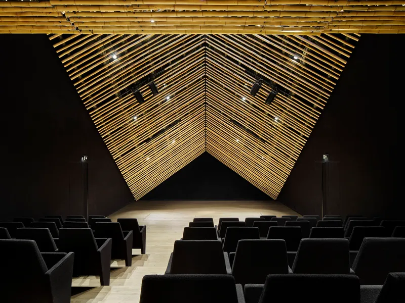 Front view of the auditorium stage with folded timber baffle ceiling forming a geometric chevron pattern