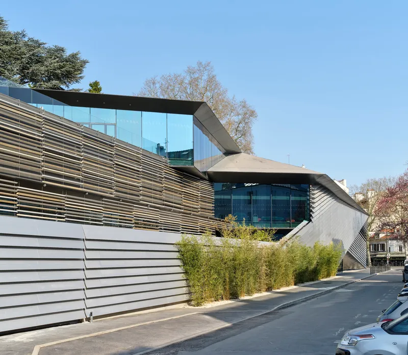 Street view of the layered horizontal louver facade with bamboo plantings under clear spring sky