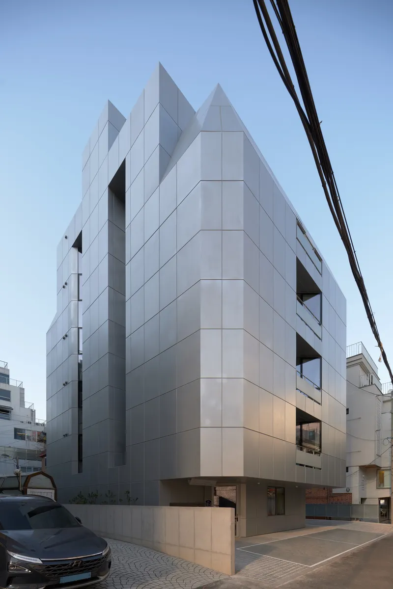 Corner view of the white paneled facade with jagged roofline and recessed openings at dusk