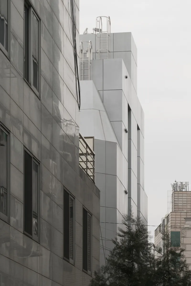 Side elevation showing the white paneled volume rising above neighboring rooftops on an overcast day