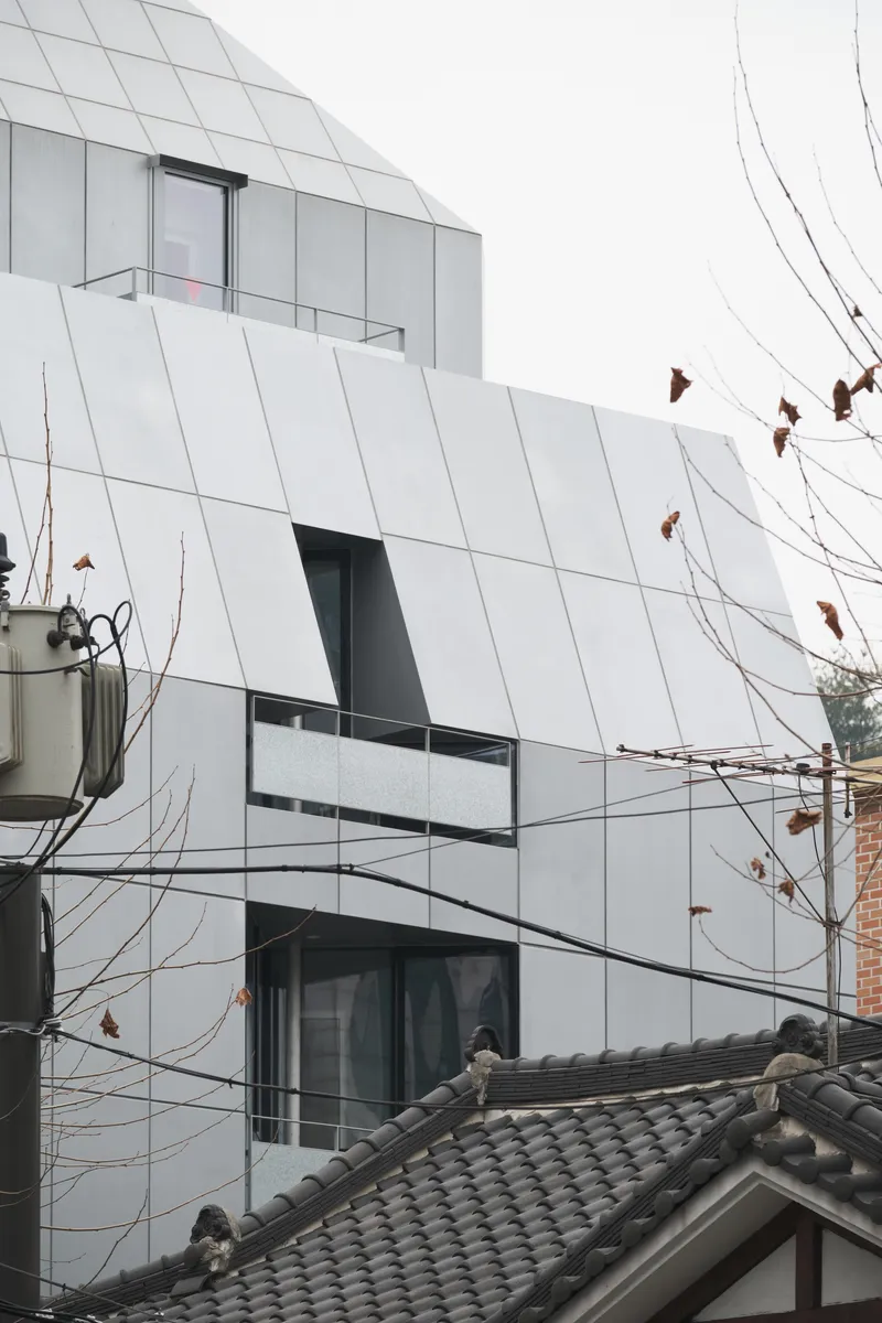 Angled white facade with recessed balconies behind bare tree branches and overhead wires