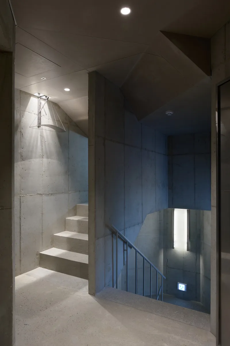 Concrete stairwell with floating treads, metal handrail and narrow vertical window illuminating the landing