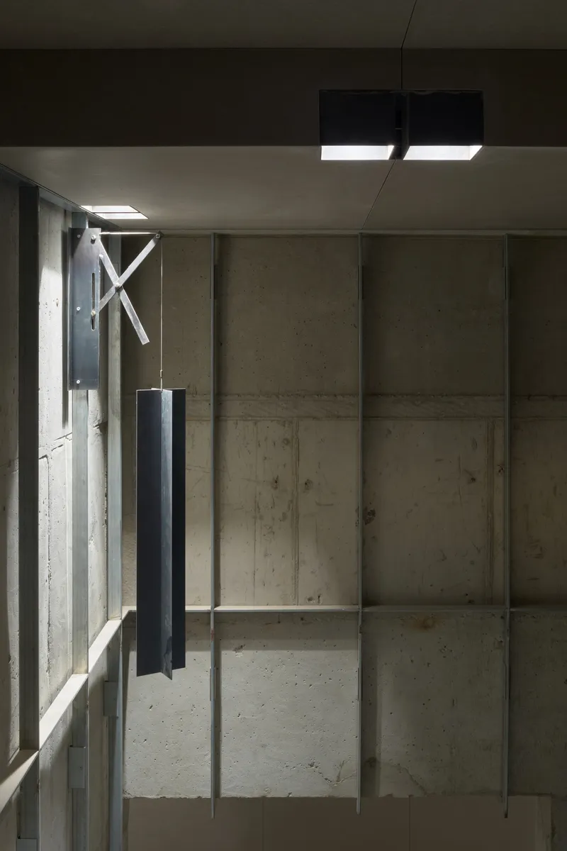 Interior view of exposed concrete wall panels with vertical steel columns and suspended lighting fixtures