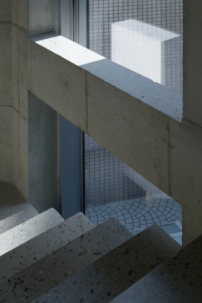 Concrete staircase with sunlight casting angular shadows on white glass block wall