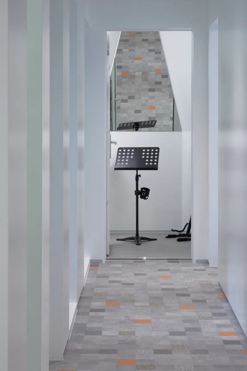 White corridor with doorway revealing patchwork tile floor with orange accents and music stand