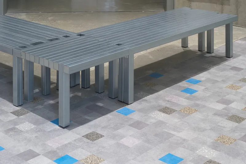 Grey slatted benches on multicolored terrazzo tile floor with blue and beige inlays
