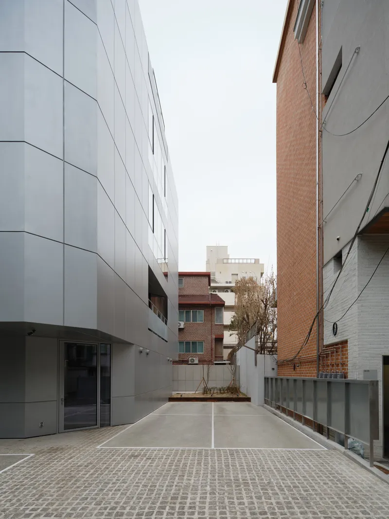 Narrow alley between white paneled facade and brick buildings with bare tree