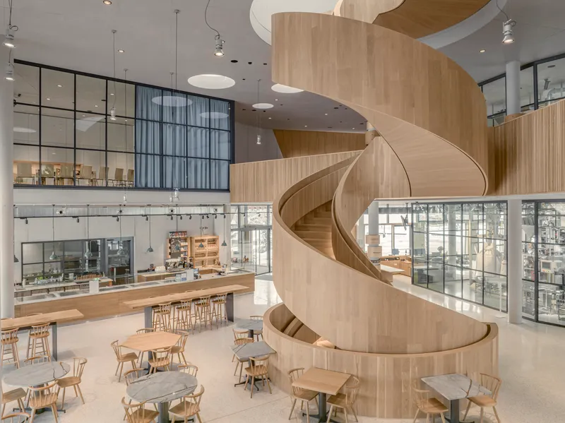 Double-height interior with spiral timber stair and cafe seating area below glazed openings