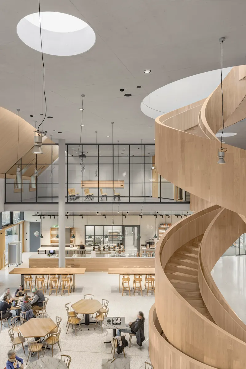 Helical timber staircase viewed from below with patrons seated at tables in the cafe