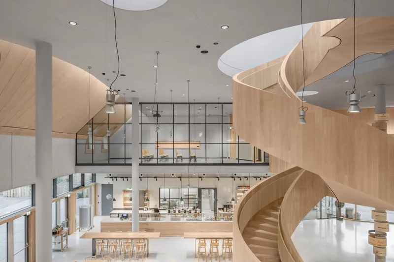 Atrium view showing mezzanine level with steel-framed glazing and curved timber stair balustrade