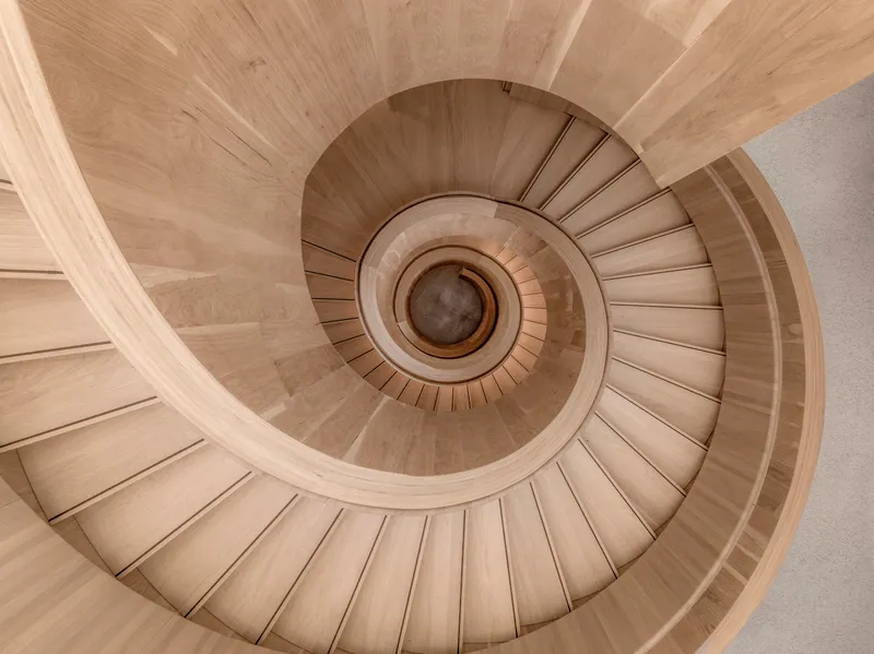 Top-down view of a spiral staircase with light timber treads and curved risers around a central void