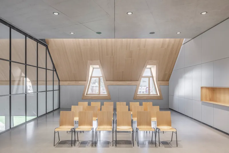 Assembly room with rows of plywood chairs beneath a ribbed timber ceiling and triangular dormer windows