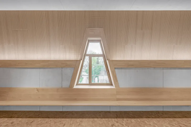 Timber bench seating along a concrete wall with a recessed triangular window framing trees outside