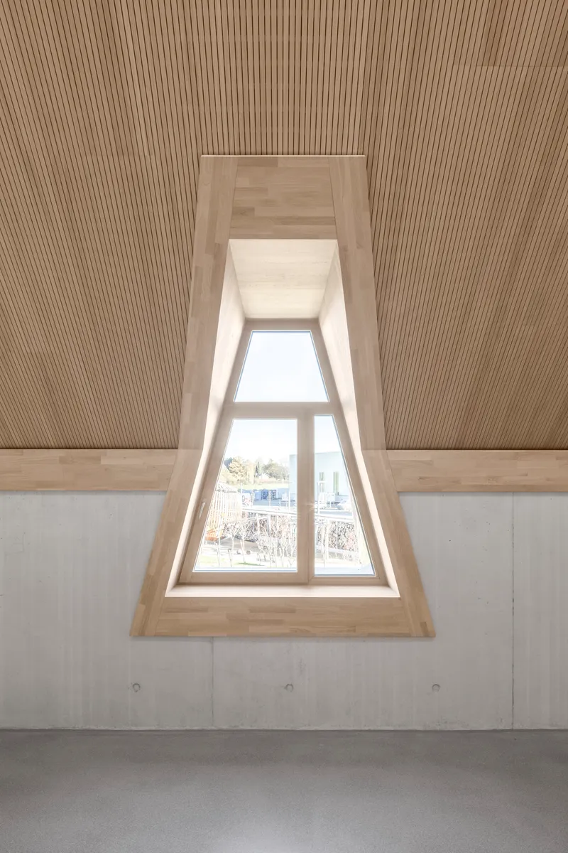 Recessed triangular dormer window with timber lining and ribbed ceiling above bare concrete walls