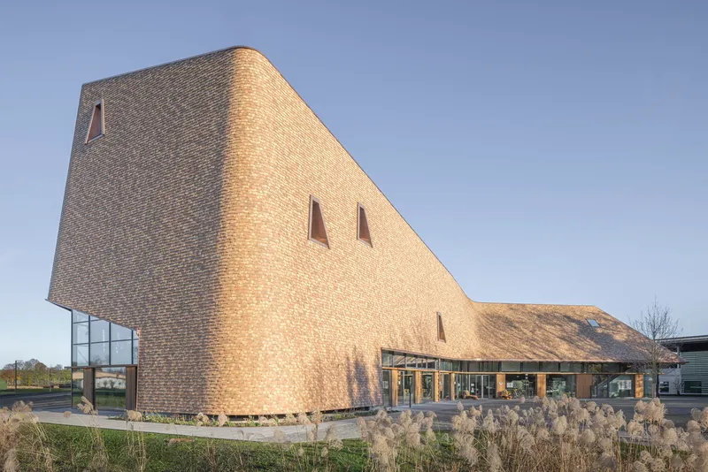 Corner detail of the faceted brick volume with tapered window openings and ornamental grasses