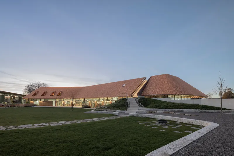 Low-angled view of the undulating shingled roof volumes across a lawn at dusk