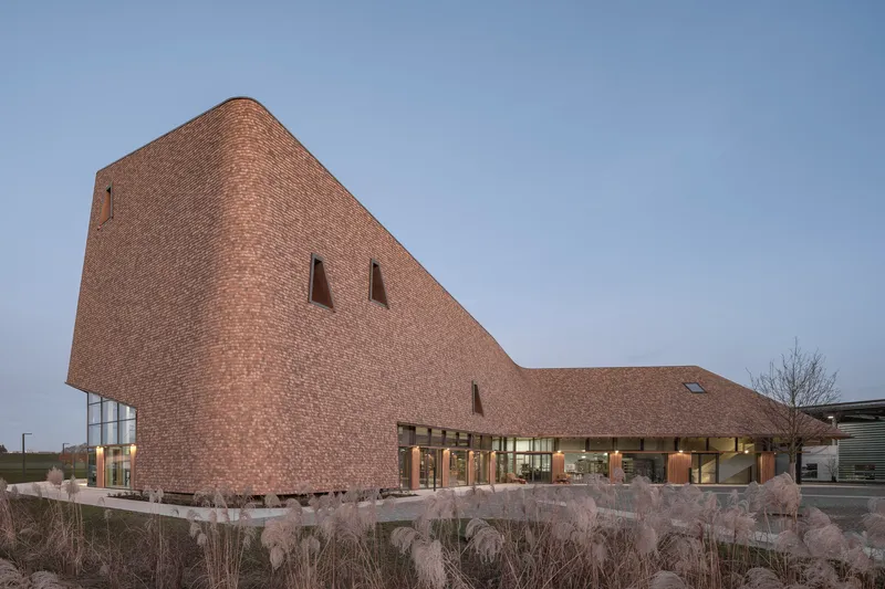 Shingled facade with narrow vertical windows above a planted bed with ornamental grasses