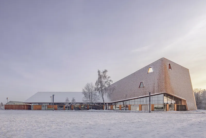 The shingled volume and linear pavilion across a frozen courtyard at dawn