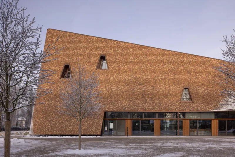 Textured brick facade with triangular openings in a winter plaza with bare trees and snow