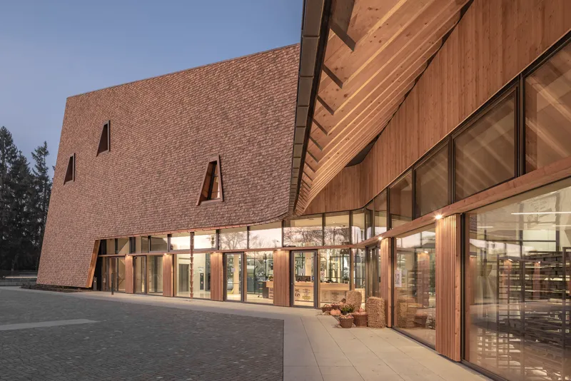 Glass entrance with timber cladding at dusk beneath the overhanging textured brick volume