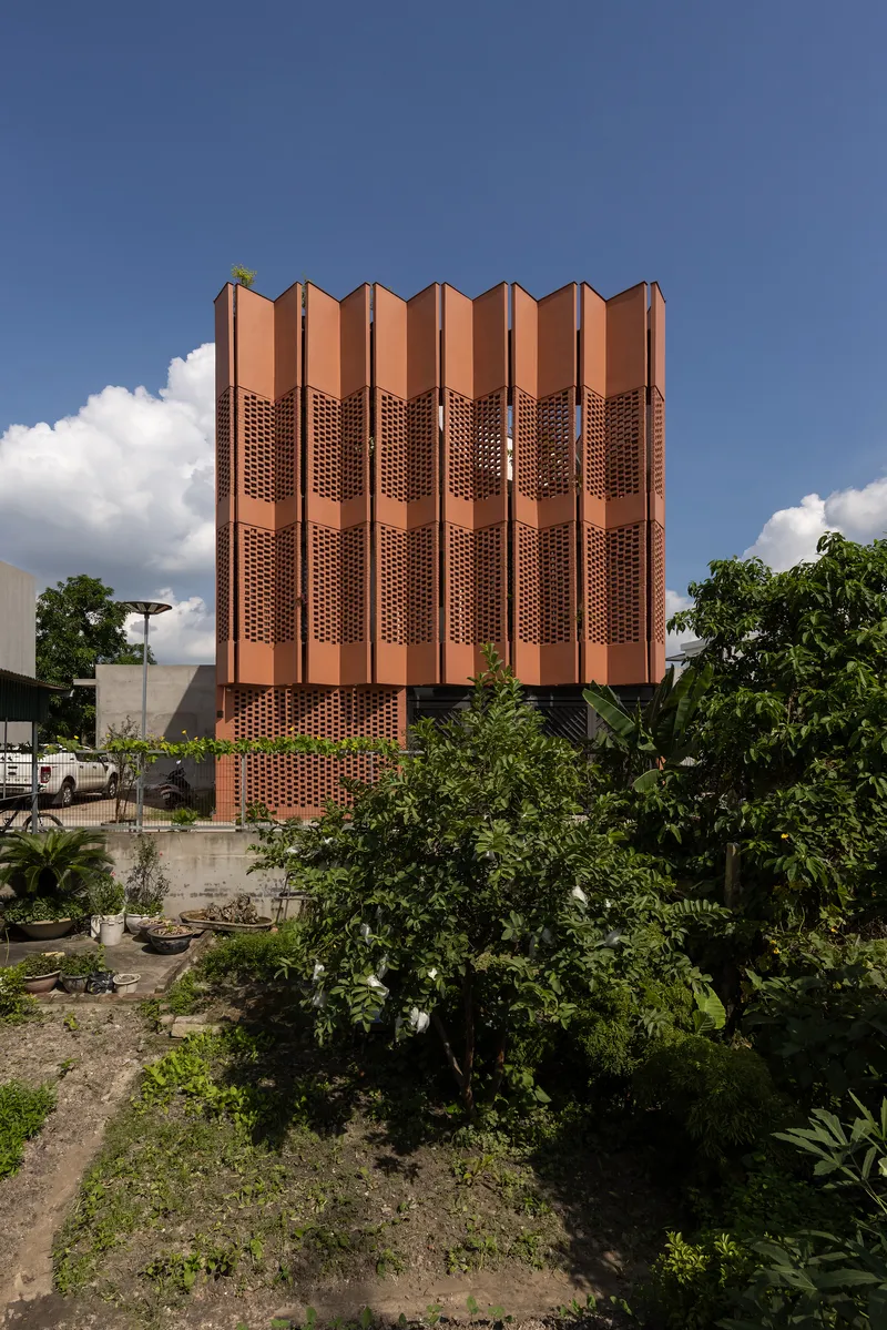 Street view of the copper-toned corrugated facade tower framed by young trees in a planted garden