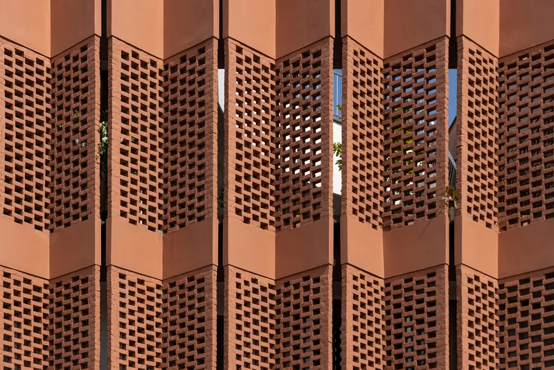 Repeating terracotta lattice panels in warm sunlight with glimpses of greenery through the openings