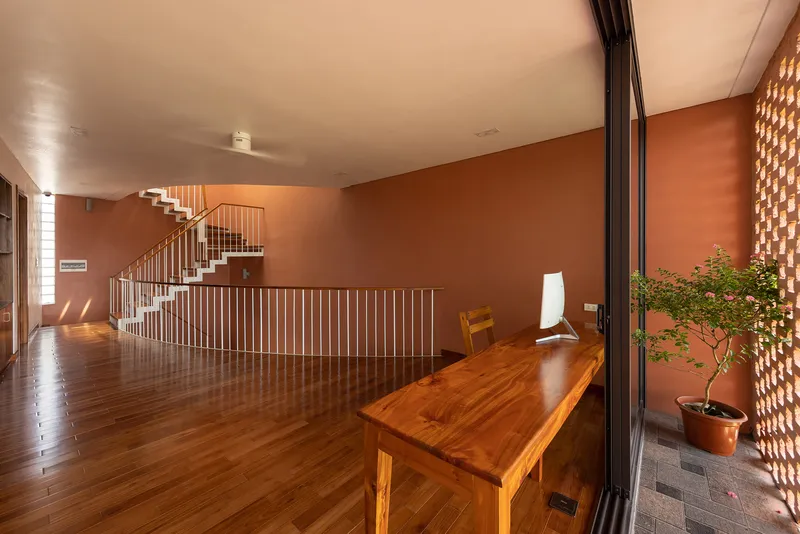 Upper floor corridor with timber desk beside a perforated screen wall and potted bonsai tree