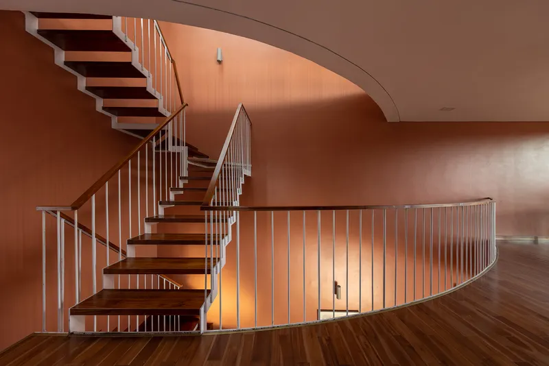 Curving timber and steel staircase with vertical balustrades against terracotta walls under diffused light