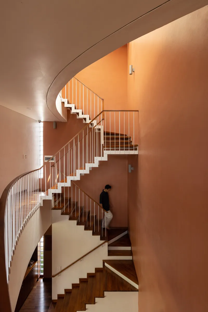Multi-level spiral staircase with figure descending past terracotta walls and slender vertical railings