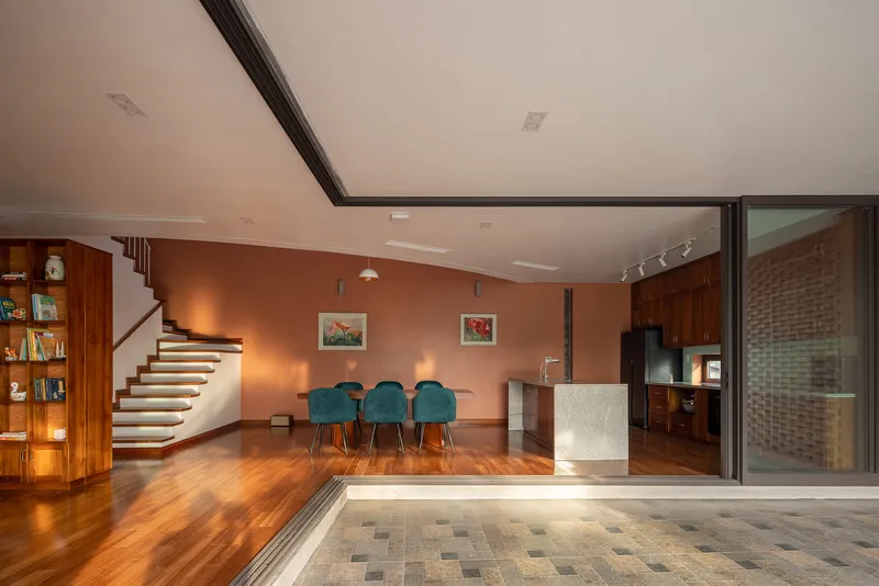 Living space opening to paved courtyard through sliding glass doors beside a curved staircase