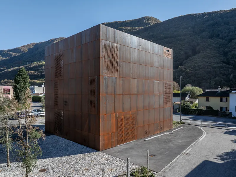 Corner view of the oxidized copper facade with perforated screens and a gravel perimeter against mountains