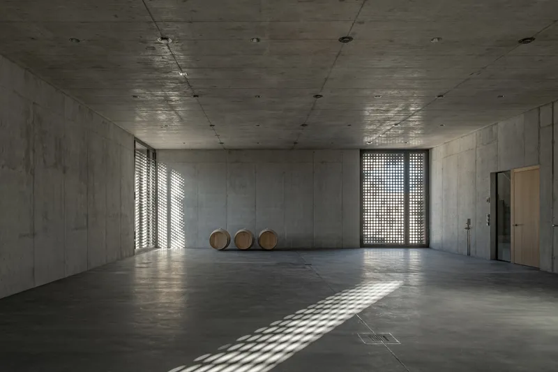 Bare concrete interior with wooden barrels and light filtering through perforated screen openings