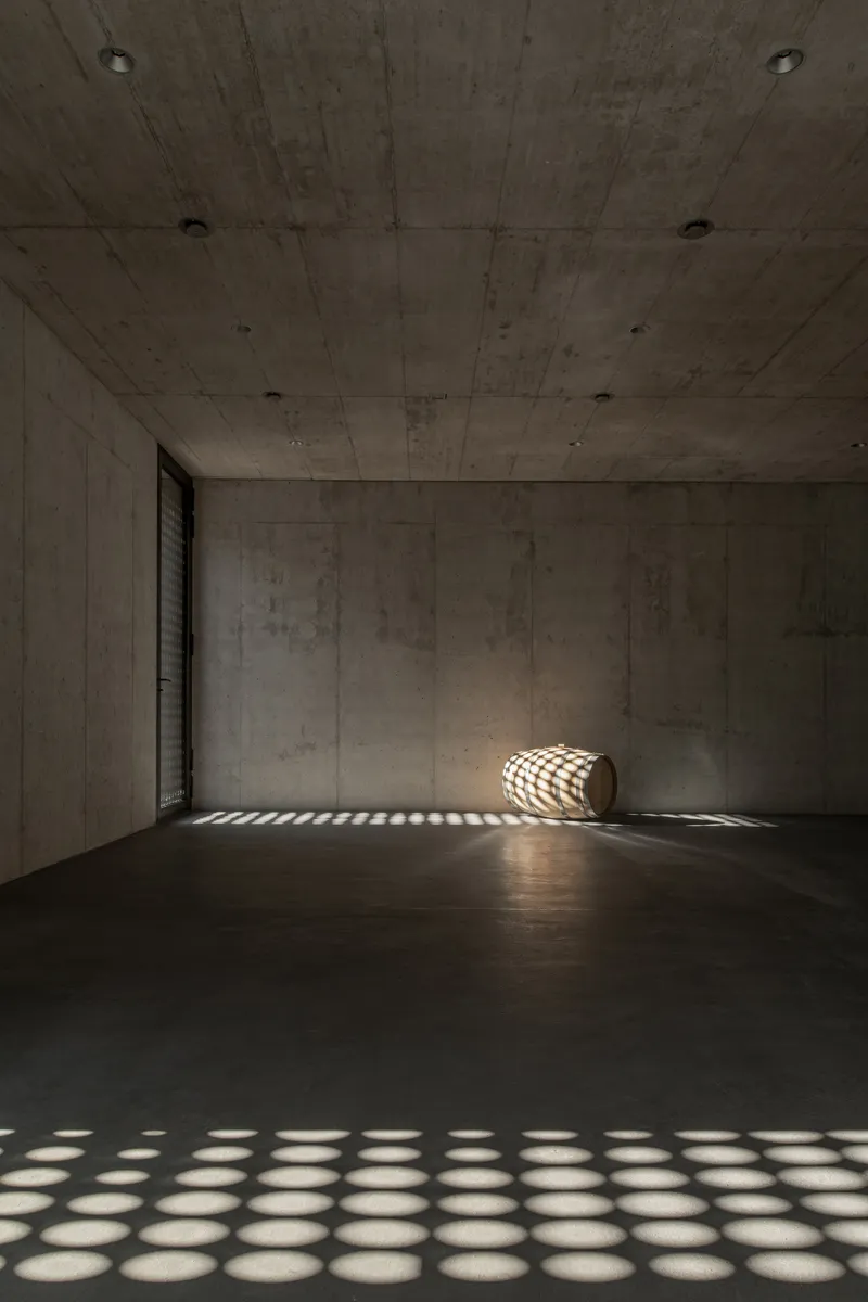 Empty concrete room with a wine barrel casting patterned shadows from a perforated screen