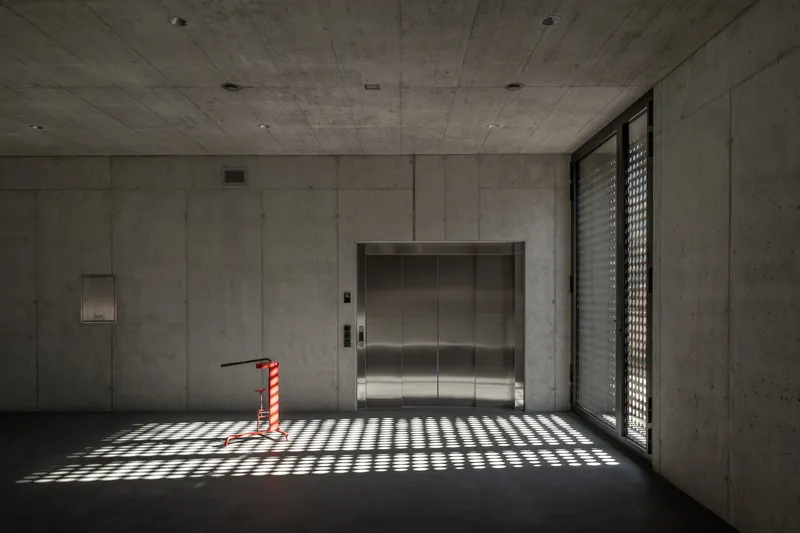 Concrete lobby with stainless steel elevator doors and patterned light from a perforated screen window