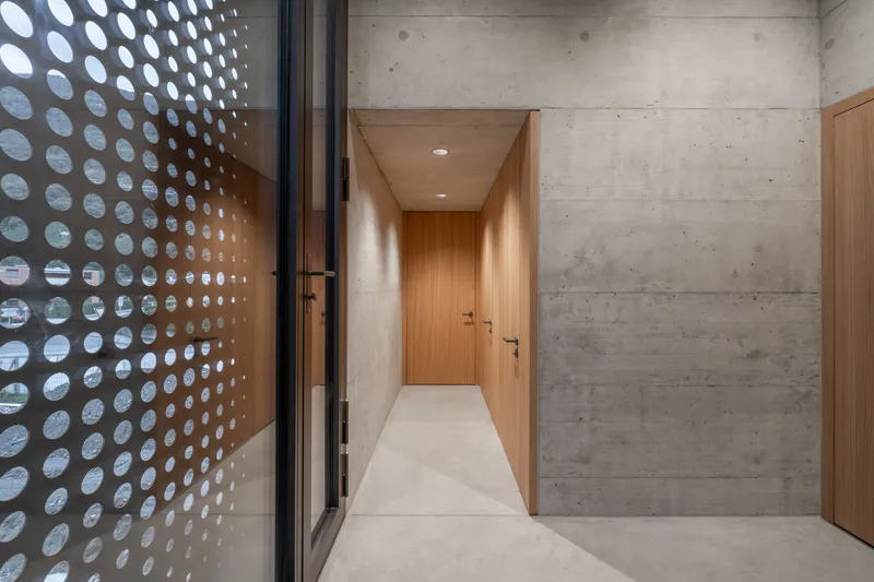 Corridor with timber-clad walls and perforated metal screen casting circular light patterns on terrazzo flooring