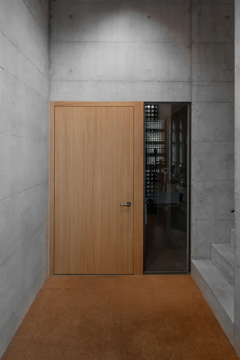 Timber door and glass panel set into board-formed concrete walls above cork flooring