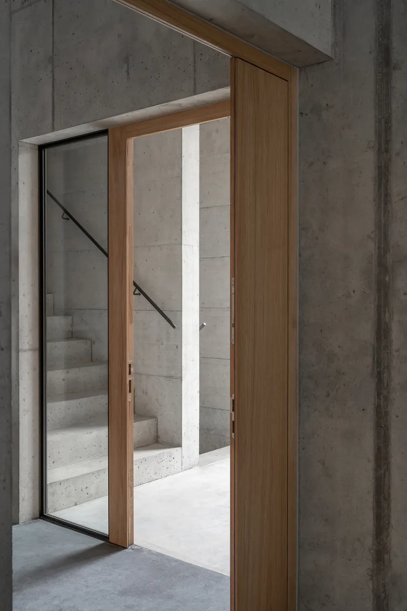 Timber-framed doorway opening to a concrete staircase with metal handrail in daylight