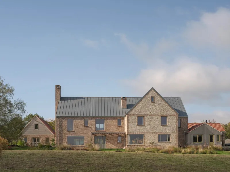Cluster of gabled brick and stone volumes with standing seam metal roofs under a partly cloudy sky