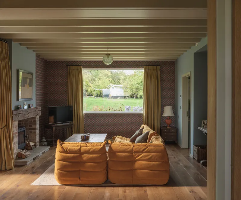 Living room with exposed timber ceiling joists and a landscape window framing green fields beyond